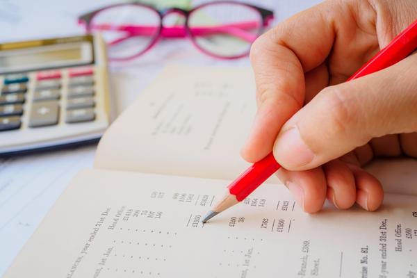 woman's hand holding a red pencil writing in budget with calculator and glasses in the background
