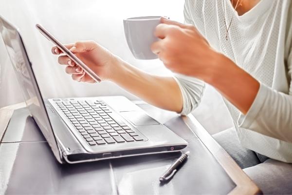 women working on phone by laptop with cup of coffee
