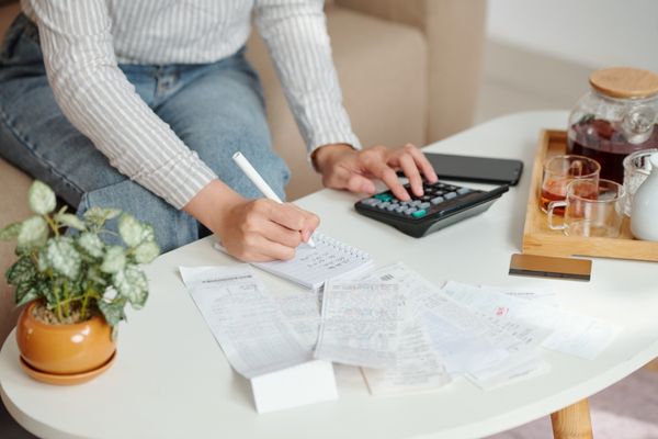Hands of woman using calculator while she checking bills and writing down figures sitting at table