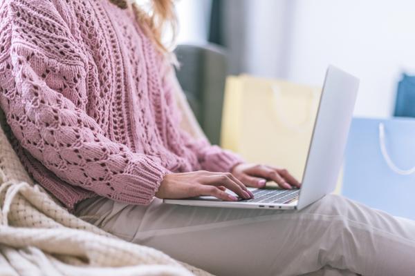 women in pink sweater sitting on sofa with laptop in lap typing