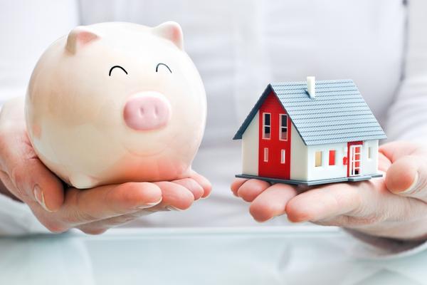woman close up holding piggy bank in one hand and a model of a toy house in the other